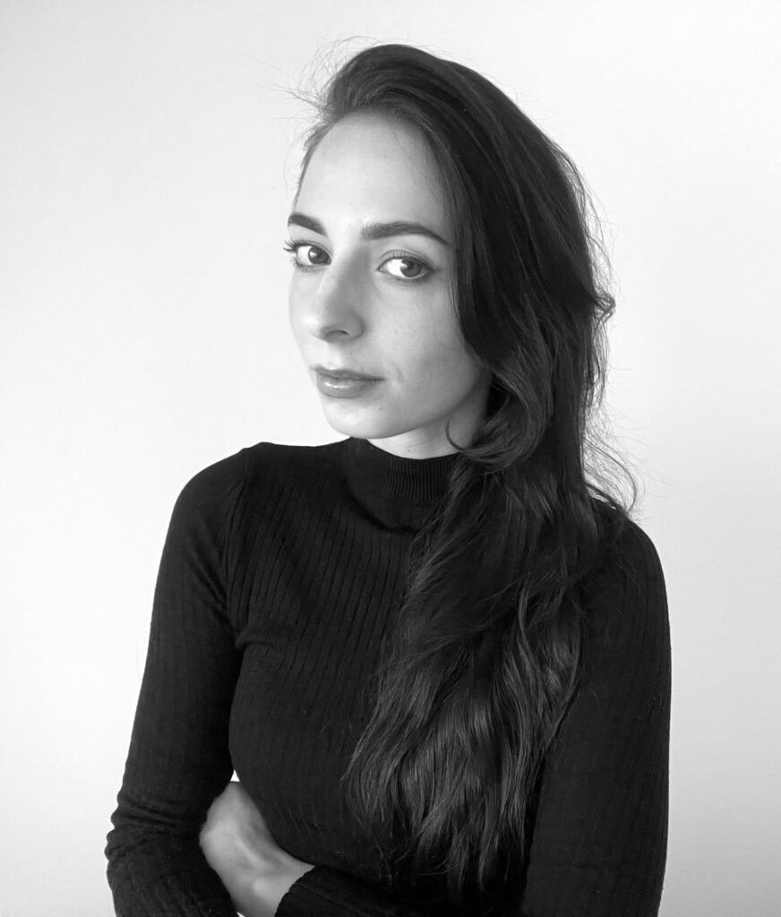 Młoda kobieta z długimi, rozpuszczonymi włosami. Zdjęcie jest czarno-białe. Ma na sobie czarną bluzkę z golfem. Za nią jest białe tło. To Adrianna Stawska, projektantka wnętrz.